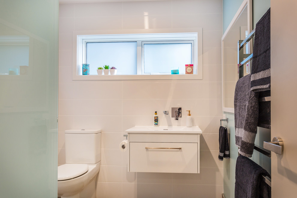 Mittelgroßes Badezimmer mit weißen Schränken, Eckdusche, Wandtoilette mit Spülkasten, weißen Fliesen, Keramikfliesen, blauer Wandfarbe, Porzellan-Bodenfliesen, Wandwaschbecken, grauem Boden und Falttür-Duschabtrennung in Auckland