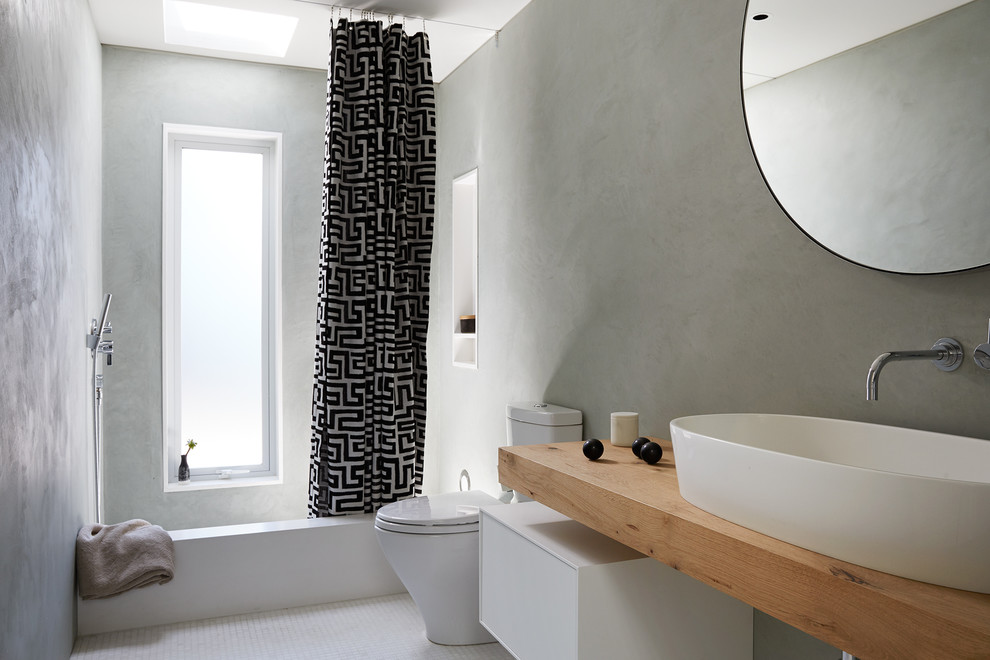 Modern inredning av ett mellanstort brun brunt en-suite badrum, med ett fristående handfat, släta luckor, vita skåp, ett badkar i en alkov, grå väggar, träbänkskiva, mosaikgolv och vitt golv