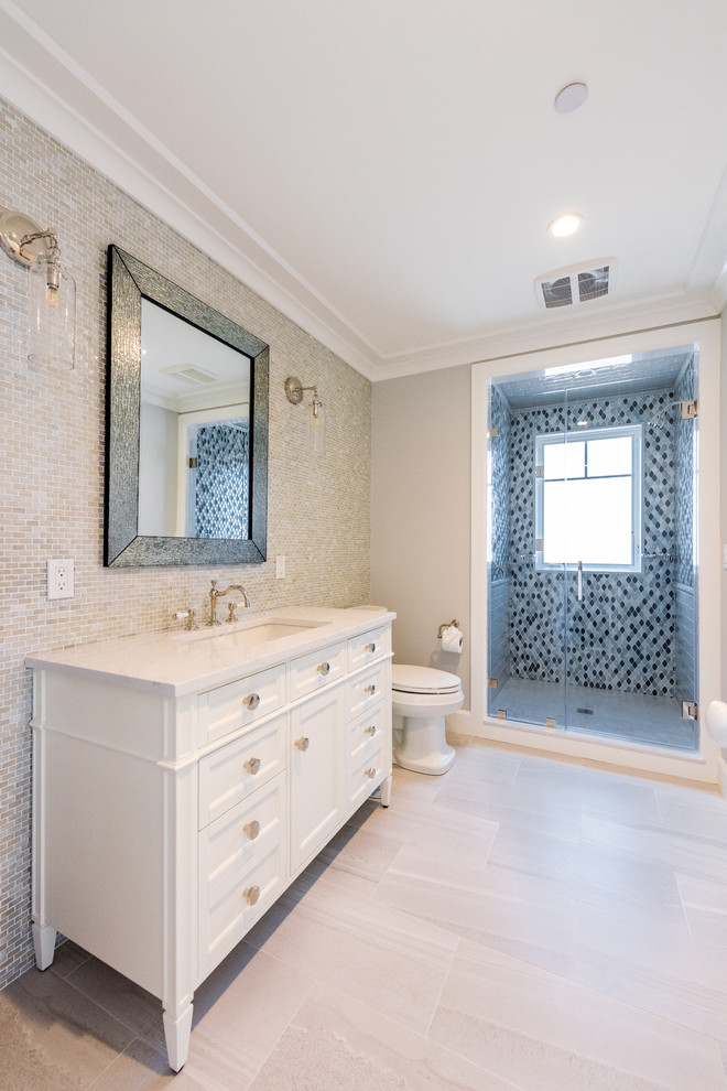Photo of a medium sized beach style shower room bathroom in New York with medium wood cabinets, an alcove shower, a one-piece toilet, green tiles, glass tiles, grey walls, vinyl flooring, an integrated sink, quartz worktops, beige floors, a hinged door, white worktops and recessed-panel cabinets.