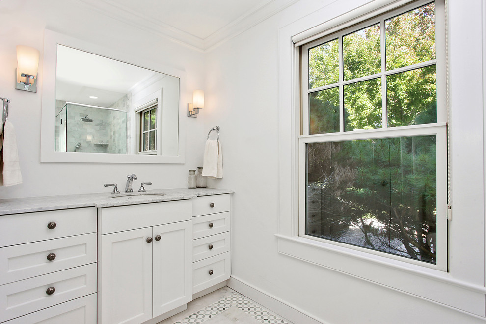 This is an example of a traditional bathroom in New York with shaker cabinets, white cabinets, an alcove shower, a one-piece toilet, white walls, mosaic tile flooring, a submerged sink and marble worktops.