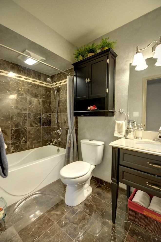 サンフランシスコにあるお手頃価格の小さなトランジショナルスタイルのおしゃれな浴室 (アンダーカウンター洗面器、落し込みパネル扉のキャビネット、黒いキャビネット、大理石の洗面台、アルコーブ型浴槽、シャワー付き浴槽	、分離型トイレ、茶色いタイル、石タイル、グレーの壁、大理石の床) の写真