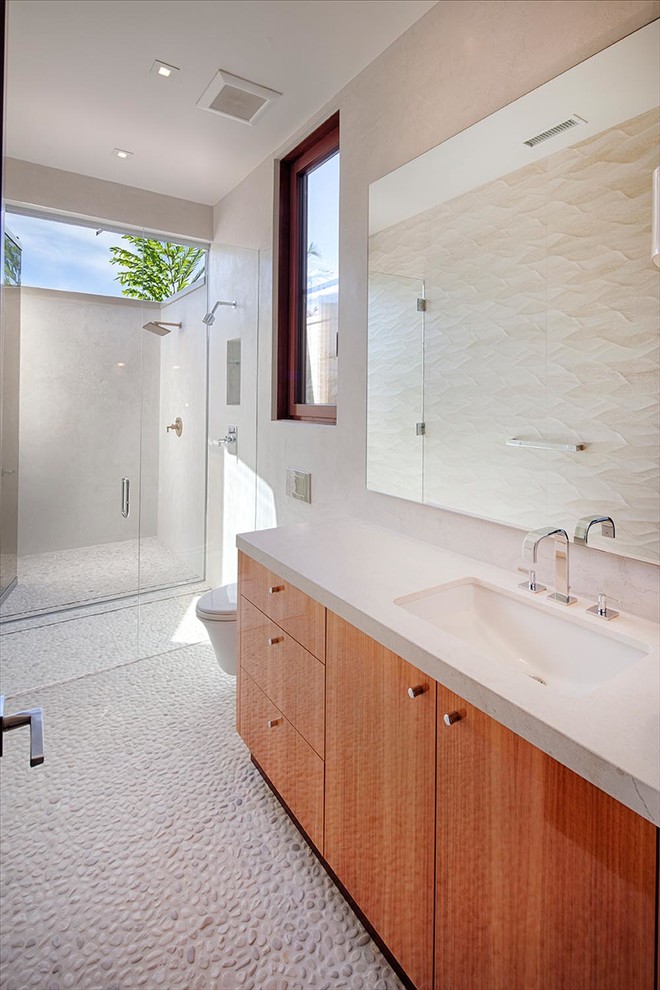 Idée de décoration pour une très grande salle de bain design en bois brun avec un lavabo encastré, un placard à porte plane, un plan de toilette en calcaire, une douche à l'italienne, WC suspendus, un carrelage multicolore, des carreaux de porcelaine, un mur blanc et un sol en galet.