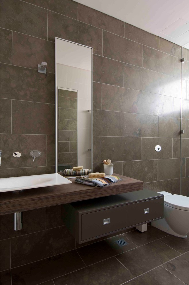 Cette image montre une salle de bain minimaliste avec une vasque, un mur marron, un sol marron et un plan de toilette marron.