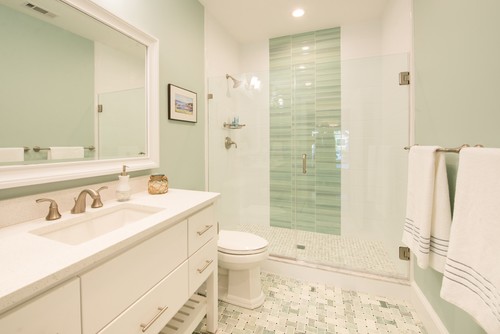 Bright bathroom with white bathroom cabinets, quartz countertop, glass shower enclosure, and mint green walls with patterned tile floor