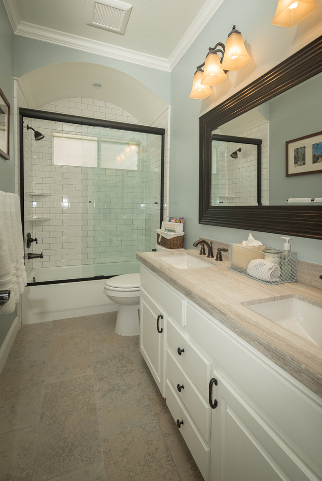Photo of a medium sized traditional bathroom in Houston with a submerged sink, flat-panel cabinets, white cabinets, limestone worktops, an alcove bath, an alcove shower, white tiles, metro tiles, blue walls and porcelain flooring.
