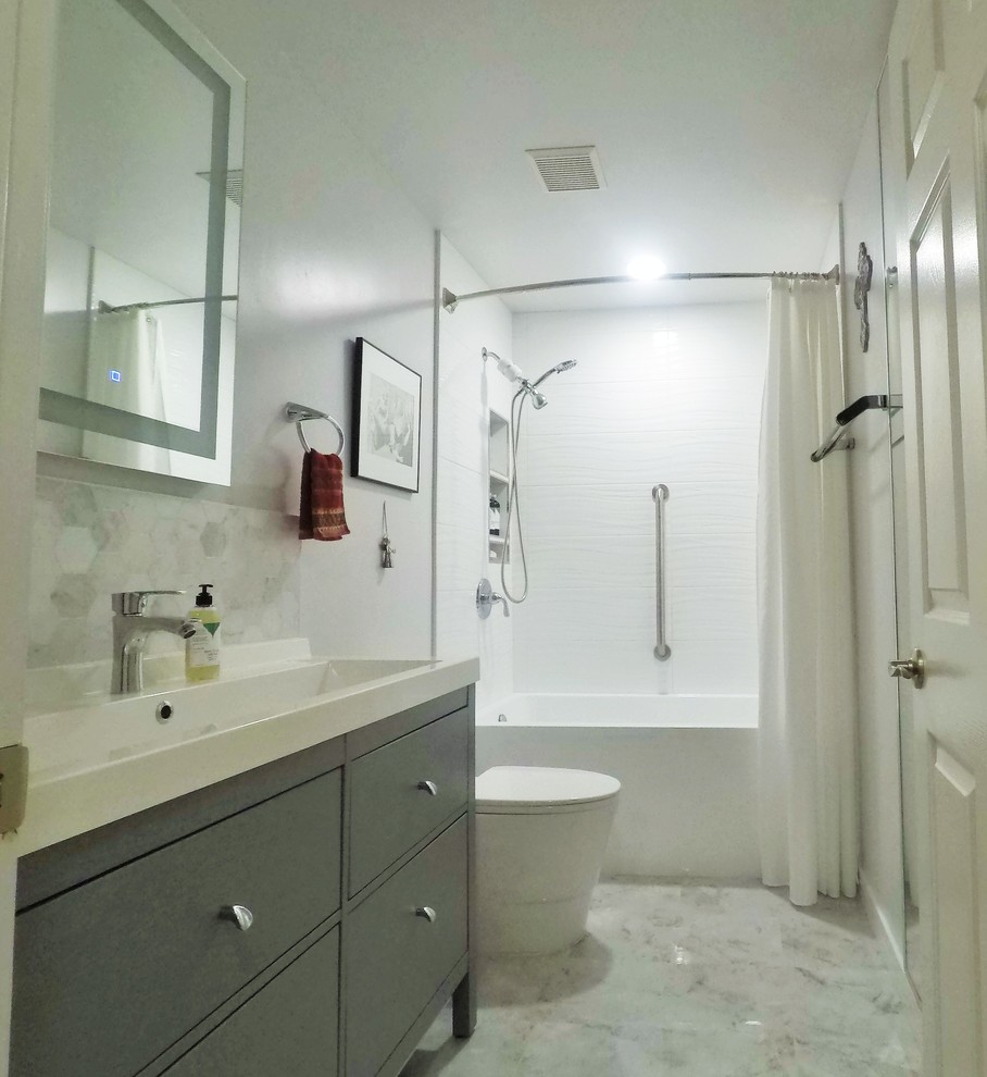 Cette photo montre une salle d'eau tendance de taille moyenne avec un placard à porte plane, des portes de placard grises, une baignoire en alcôve, un combiné douche/baignoire, WC à poser, un carrelage blanc, des carreaux de céramique, un mur gris, un sol en carrelage de porcelaine, une grande vasque, un plan de toilette en surface solide, un sol gris, une cabine de douche avec un rideau et un plan de toilette blanc.