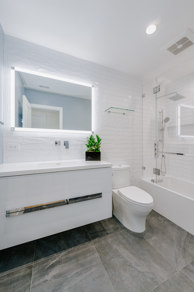 Réalisation d'une salle de bain design de taille moyenne pour enfant avec un placard en trompe-l'oeil, des portes de placard blanches, une baignoire d'angle, un combiné douche/baignoire, WC à poser, des carreaux de porcelaine, un mur blanc, un sol en carrelage de porcelaine, un lavabo intégré, un sol gris et un plan de toilette blanc.