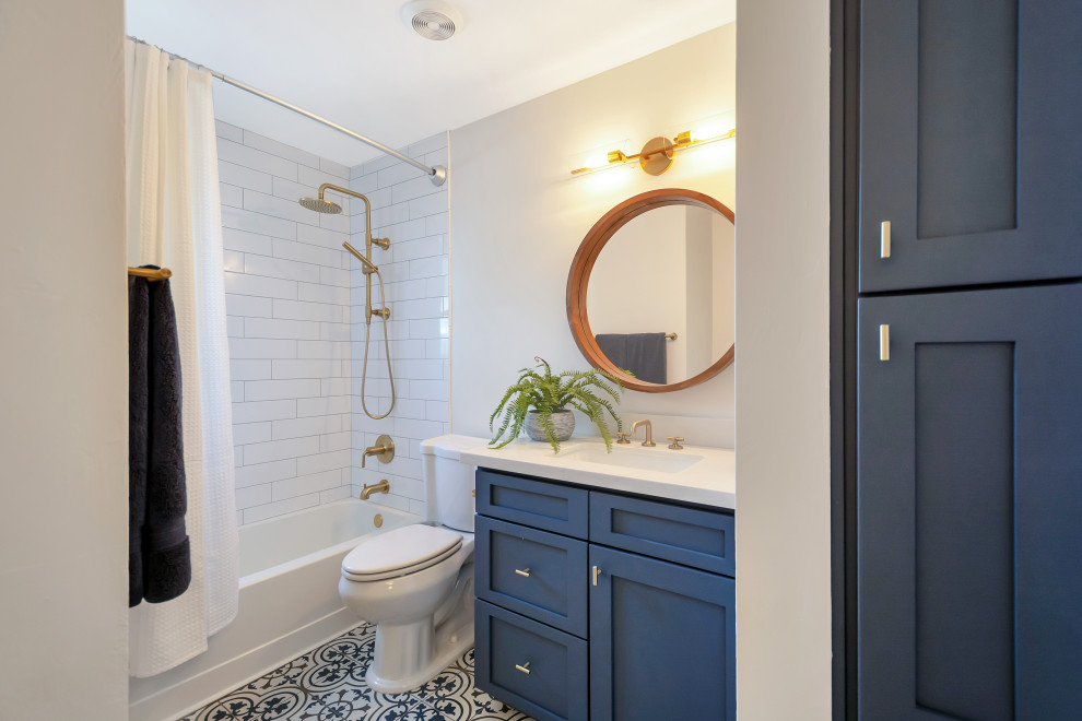 Пример оригинального дизайна: маленькая ванная комната в стиле неоклассика (современная классика) с фасадами в стиле шейкер, синими фасадами, ванной в нише, душем над ванной, белой плиткой, плиткой кабанчик, серыми стенами, полом из керамогранита, врезной раковиной, столешницей из искусственного кварца, шторкой для ванной, белой столешницей, тумбой под одну раковину, встроенной тумбой, разноцветным полом и душевой кабиной для на участке и в саду