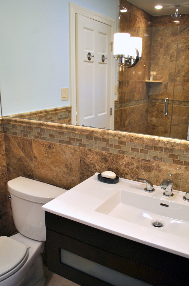 Photo of a medium sized contemporary ensuite bathroom in Philadelphia with a wall-mounted sink, glass-front cabinets, dark wood cabinets, ceramic flooring, an alcove shower, a two-piece toilet, beige tiles, brown tiles, stone tiles, beige walls and solid surface worktops.