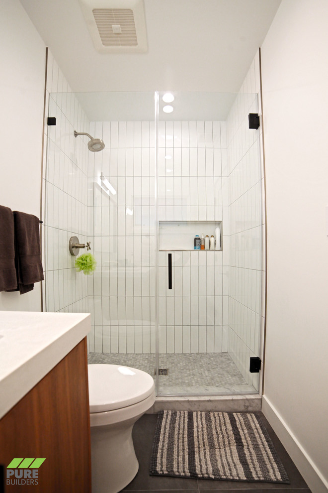 Идея дизайна: маленькая ванная комната в стиле модернизм с плоскими фасадами, темными деревянными фасадами, душем в нише, унитазом-моноблоком, белой плиткой, керамической плиткой, белыми стенами, полом из керамической плитки, душевой кабиной, врезной раковиной, столешницей из искусственного камня, черным полом, душем с распашными дверями и белой столешницей для на участке и в саду