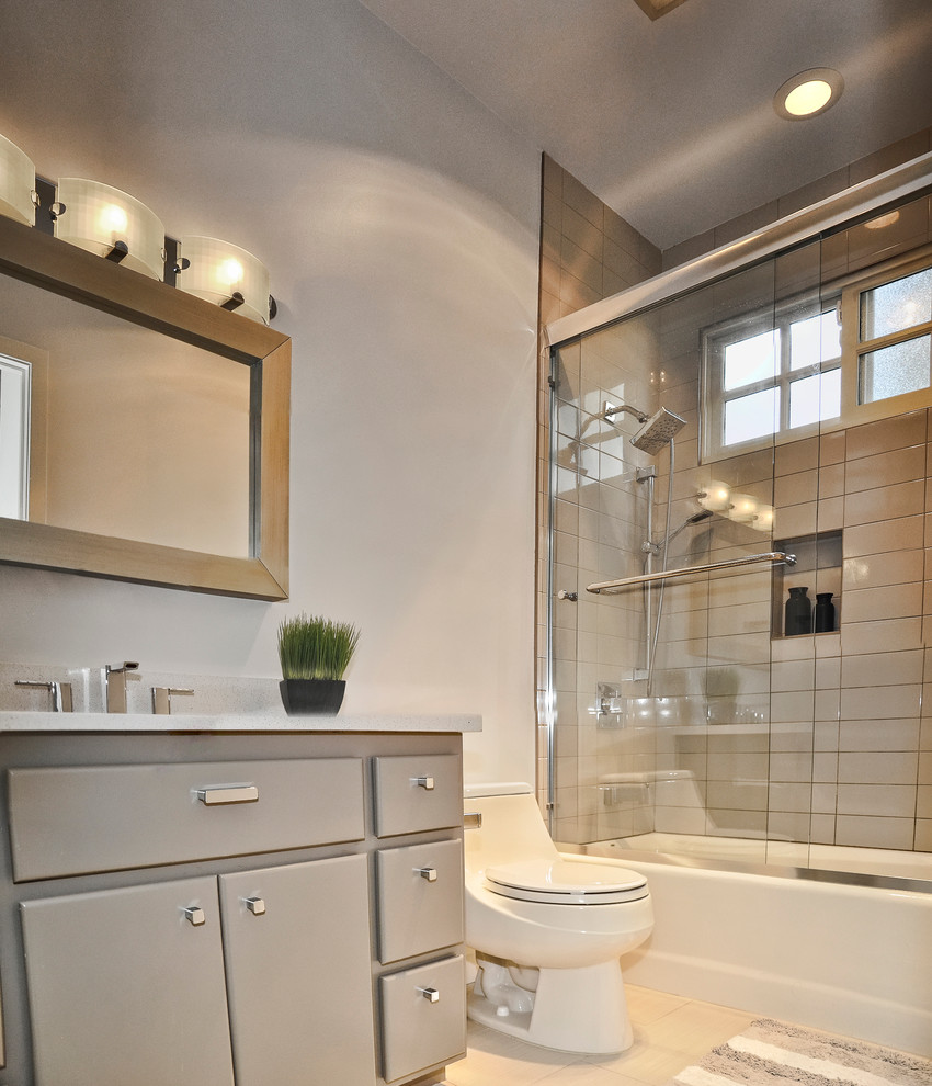 Cette image montre une petite salle de bain design avec un lavabo encastré, un placard à porte plane, des portes de placard grises, un plan de toilette en quartz modifié, un combiné douche/baignoire, WC à poser, un carrelage métro, un mur gris, un sol en carrelage de porcelaine et un carrelage gris.