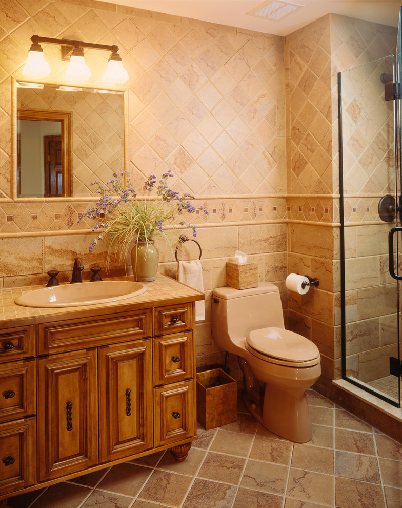 Bild på ett mellanstort amerikanskt badrum med dusch, med möbel-liknande, skåp i mellenmörkt trä, en dusch i en alkov, en toalettstol med hel cisternkåpa, beige kakel, porslinskakel, beige väggar, klinkergolv i porslin, ett nedsänkt handfat och kaklad bänkskiva