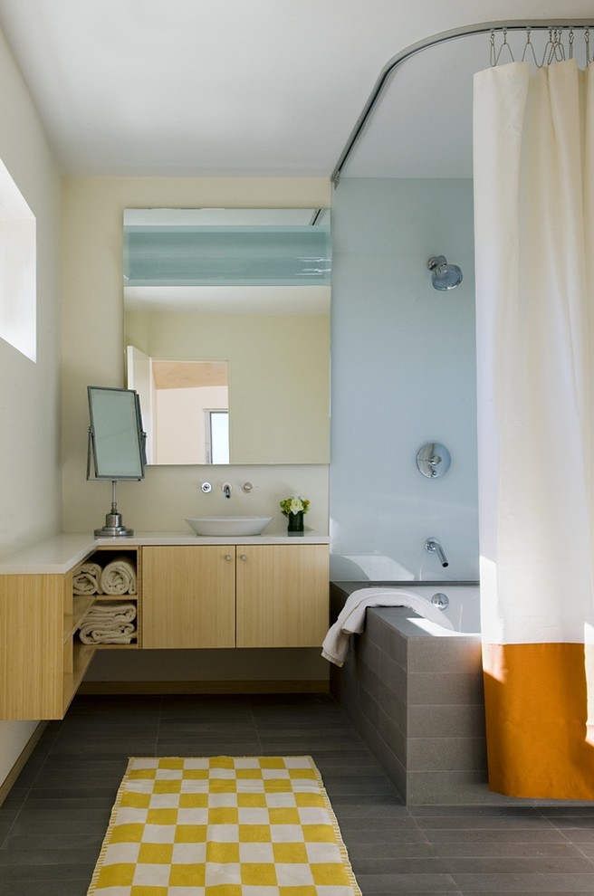 На фото: ванная комната в стиле модернизм с настольной раковиной, плоскими фасадами, светлыми деревянными фасадами, душем над ванной, серой плиткой и полновстраиваемой ванной с