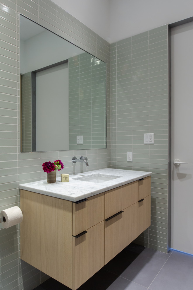 Modelo de cuarto de baño moderno con armarios con paneles lisos, puertas de armario de madera clara, baldosas y/o azulejos verdes, paredes blancas, lavabo bajoencimera, suelo gris y encimeras blancas