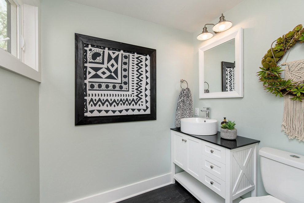 Small farmhouse 3/4 white tile dark wood floor and black floor bathroom photo in Indianapolis with furniture-like cabinets, white cabinets, a two-piece toilet, green walls, a vessel sink, glass countertops and black countertops