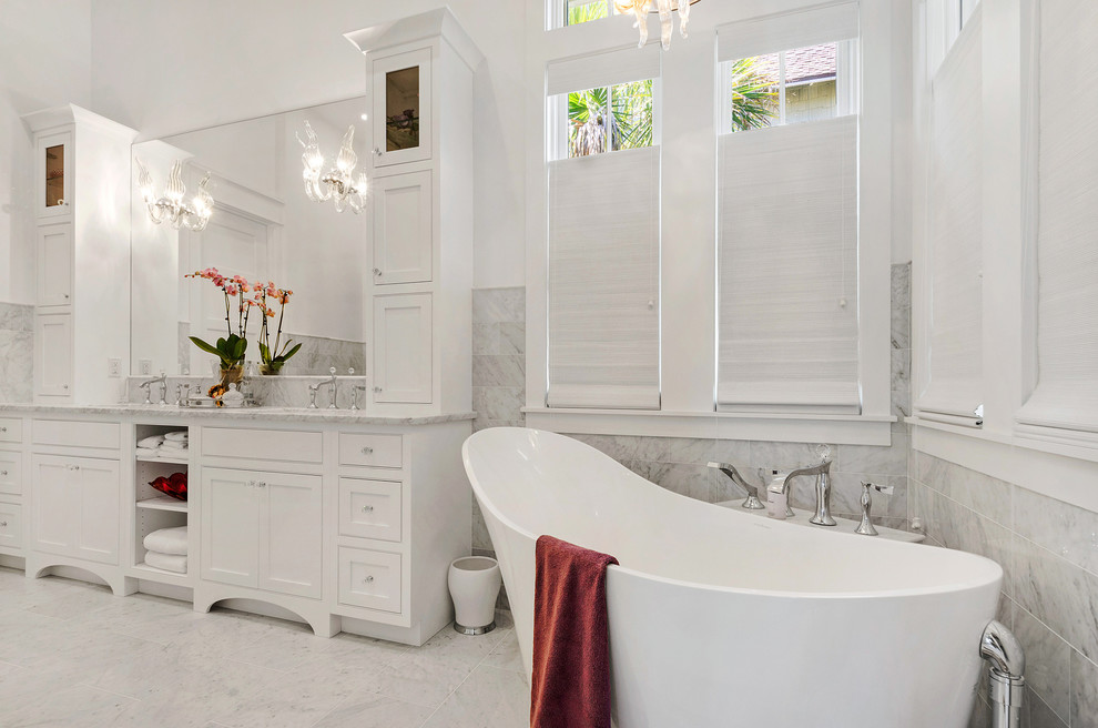 Diseño de cuarto de baño principal clásico renovado grande con armarios estilo shaker, puertas de armario blancas, bañera exenta, paredes blancas, suelo de mármol, lavabo bajoencimera, encimera de mármol y suelo blanco