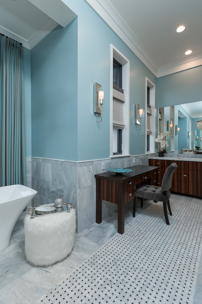 Modelo de cuarto de baño marinero con puertas de armario de madera en tonos medios, bañera exenta, encimera de mármol, sanitario de una pieza, paredes azules, suelo de mármol y lavabo bajoencimera