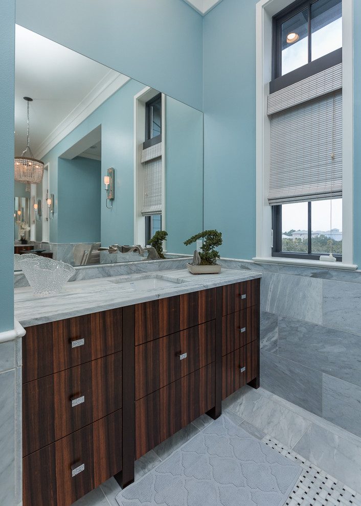 Imagen de cuarto de baño marinero con puertas de armario de madera en tonos medios, bañera exenta, sanitario de una pieza, paredes azules, suelo de mármol, lavabo bajoencimera y encimera de mármol