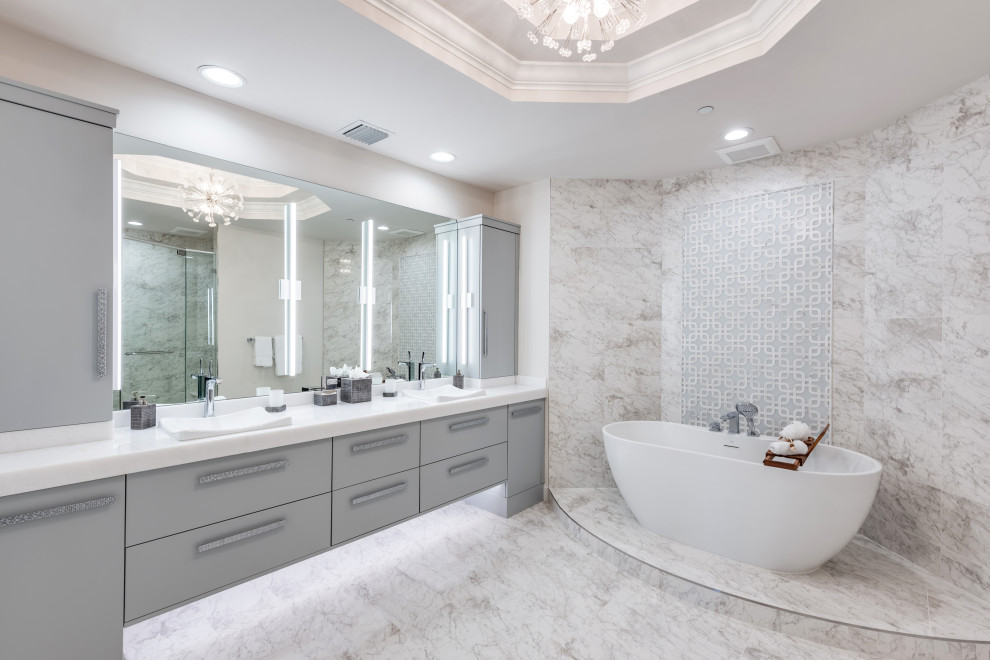 Cette photo montre une salle de bain tendance avec un placard à porte plane, des portes de placard grises, une baignoire indépendante, un carrelage gris, un lavabo posé, un sol gris, un plan de toilette blanc, meuble double vasque, meuble-lavabo encastré et un plafond décaissé.