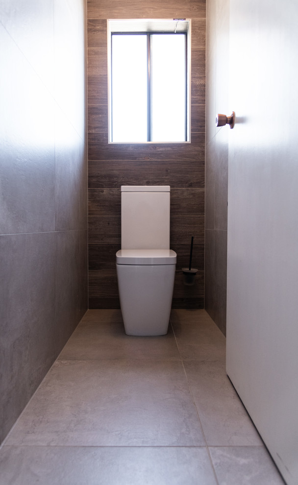 Idée de décoration pour un WC et toilettes design de taille moyenne avec un placard à porte plane, des portes de placard noires, WC à poser, un carrelage gris, des carreaux de béton, un mur gris, carreaux de ciment au sol, un lavabo intégré, un plan de toilette en calcaire, un sol gris et un plan de toilette blanc.