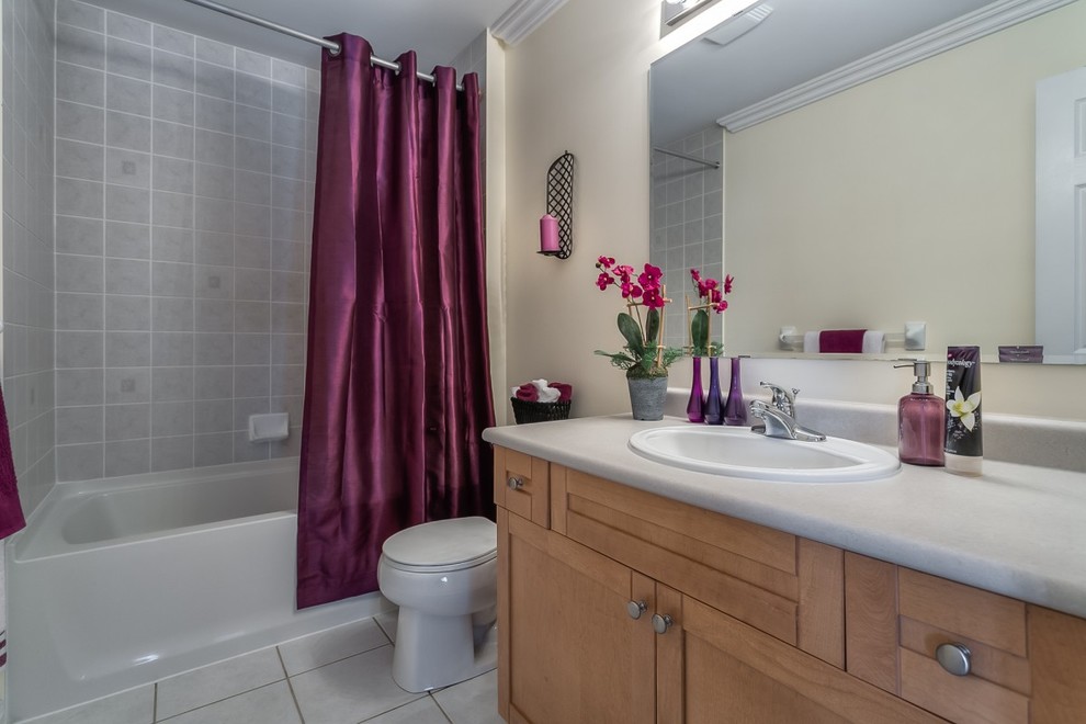 Klassisk inredning av ett litet badrum, med ett konsol handfat, luckor med profilerade fronter, skåp i ljust trä, laminatbänkskiva, ett undermonterat badkar, en dusch/badkar-kombination, en toalettstol med hel cisternkåpa, grå kakel, keramikplattor, grå väggar och klinkergolv i keramik