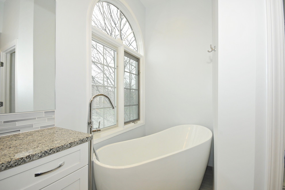 Inspiration for a medium sized contemporary ensuite bathroom in Indianapolis with white cabinets, a freestanding bath, an alcove shower, a two-piece toilet, white tiles, porcelain tiles, white walls, ceramic flooring, a submerged sink and granite worktops.