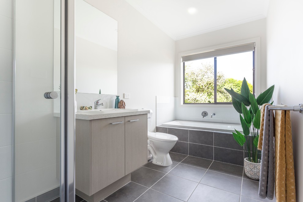 Modernes Badezimmer mit flächenbündigen Schrankfronten, hellen Holzschränken, Einbaubadewanne, weißen Fliesen, weißer Wandfarbe, Einbauwaschbecken, grauem Boden und weißer Waschtischplatte in Melbourne