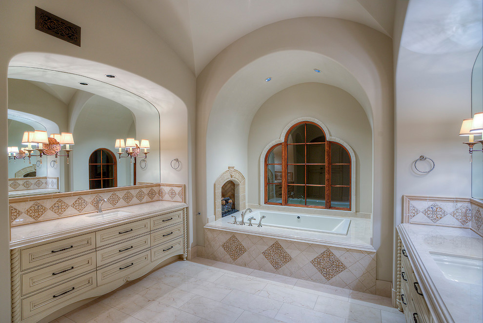 Источник вдохновения для домашнего уюта: огромная главная ванная комната в средиземноморском стиле с бежевыми фасадами, ванной в нише, угловым душем, унитазом-моноблоком, белой плиткой, плиткой мозаикой, белыми стенами, полом из травертина, монолитной раковиной, столешницей из гранита и фасадами с декоративным кантом
