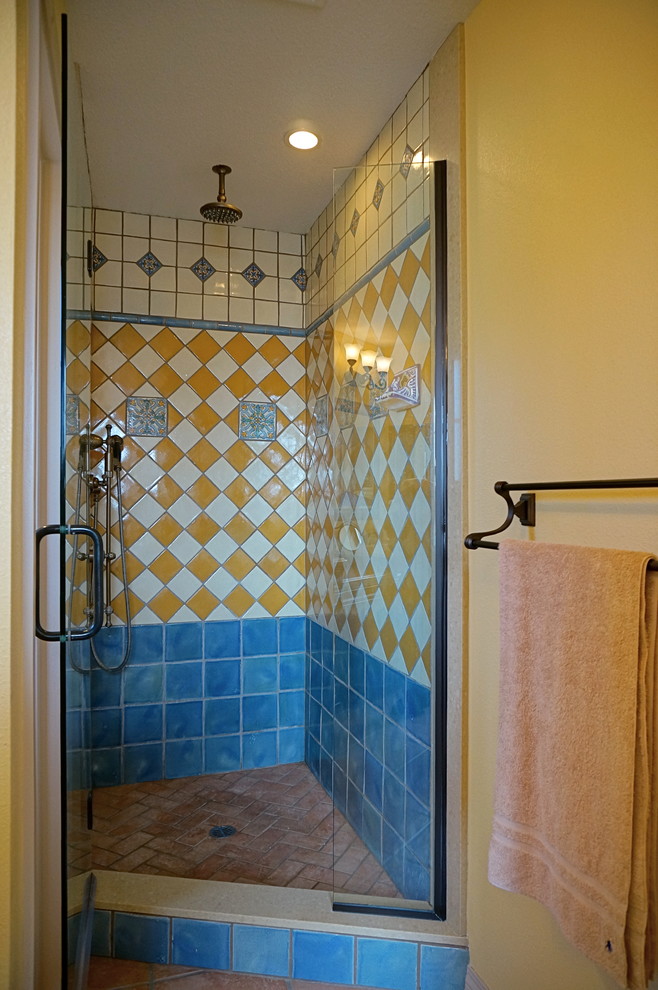 На фото: главная ванная комната в средиземноморском стиле с фасадами с утопленной филенкой, фасадами цвета дерева среднего тона, душем в нише, синей плиткой, керамической плиткой, желтыми стенами, полом из терракотовой плитки, врезной раковиной, столешницей из искусственного кварца, розовым полом, душем с распашными дверями и бежевой столешницей с
