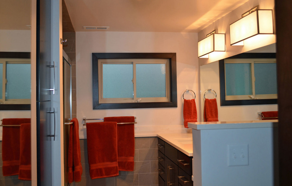 Bild på ett 50 tals badrum, med ett undermonterad handfat, släta luckor, skåp i mörkt trä, bänkskiva i kvarts, grå kakel, keramikplattor, vita väggar och klinkergolv i keramik