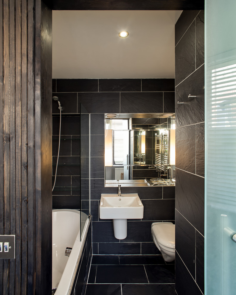 Small classic family bathroom in London with flat-panel cabinets, a built-in bath, a shower/bath combination, a wall mounted toilet, black tiles, ceramic tiles, beige walls, ceramic flooring, a wall-mounted sink, tiled worktops, black floors, an open shower and black worktops.
