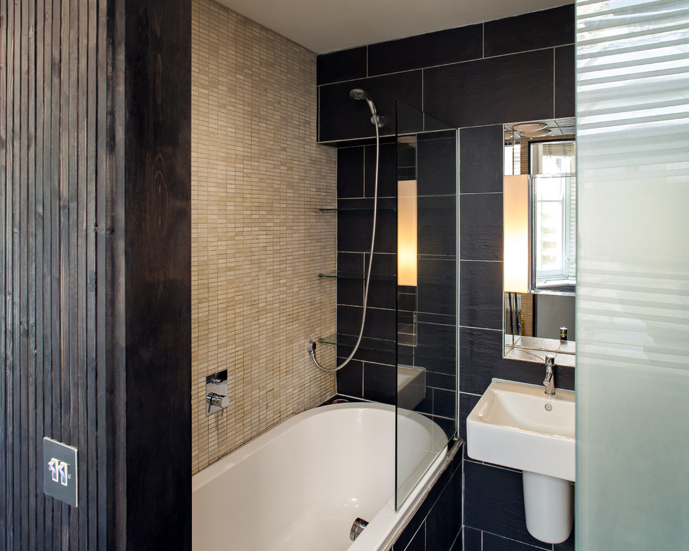 Inspiration for a small classic family bathroom in London with flat-panel cabinets, a built-in bath, a shower/bath combination, a wall mounted toilet, black tiles, ceramic tiles, beige walls, ceramic flooring, a wall-mounted sink, tiled worktops, black floors, an open shower and black worktops.