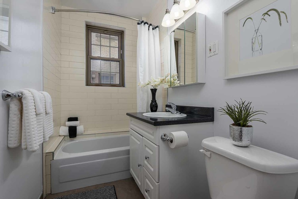 This is an example of a small contemporary ensuite bathroom in Montreal with raised-panel cabinets, white cabinets, a shower/bath combination, a two-piece toilet, yellow tiles, ceramic tiles, white walls, ceramic flooring, a built-in sink and engineered stone worktops.
