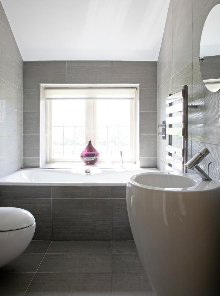 Diseño de cuarto de baño actual de tamaño medio con bañera encastrada, sanitario de pared, baldosas y/o azulejos grises, baldosas y/o azulejos de porcelana, paredes grises, suelo de baldosas de porcelana y lavabo con pedestal