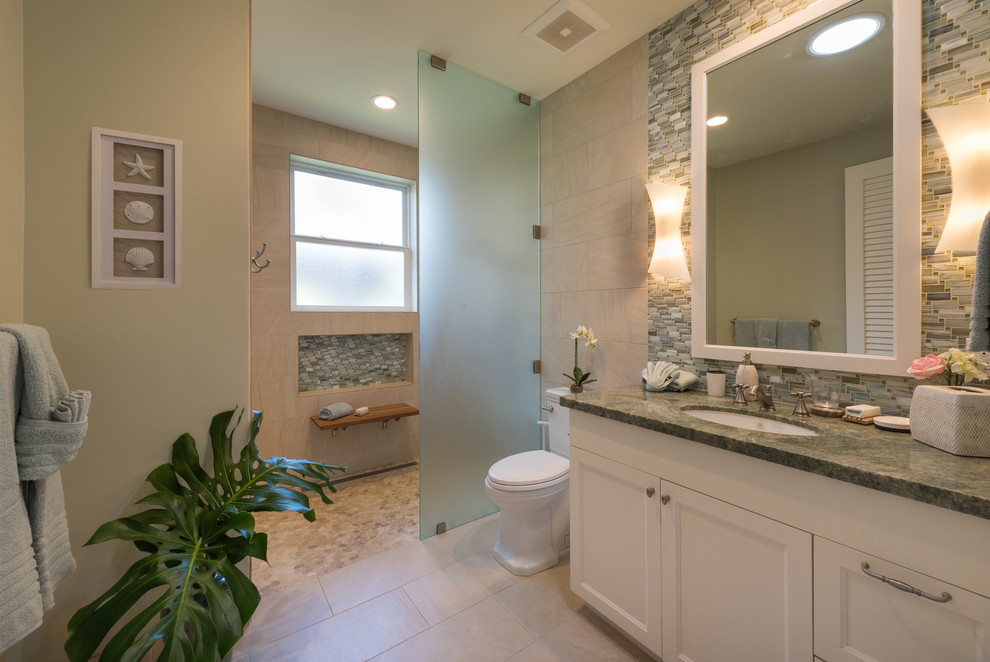 Cette photo montre une salle de bain bord de mer avec un placard à porte shaker, des portes de placard blanches, WC à poser, un carrelage vert, un carrelage en pâte de verre, un mur gris, un sol en carrelage de porcelaine, un lavabo encastré, un plan de toilette en granite et un plan de toilette vert.