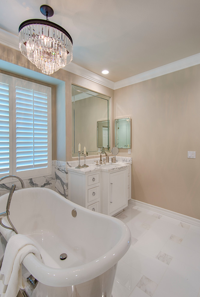 Klassisk inredning av ett stort en-suite badrum, med ett fristående badkar, en öppen dusch, marmorgolv, marmorbänkskiva, dusch med gångjärnsdörr, vitt golv, luckor med profilerade fronter, vita skåp och beige väggar