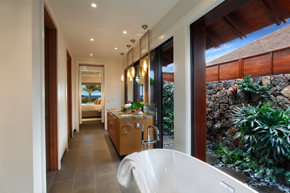 Photo of a medium sized world-inspired bathroom in Hawaii with flat-panel cabinets, medium wood cabinets, a freestanding bath, an alcove shower, a one-piece toilet, white tiles, porcelain tiles, white walls, a submerged sink, granite worktops, grey floors and multi-coloured worktops.