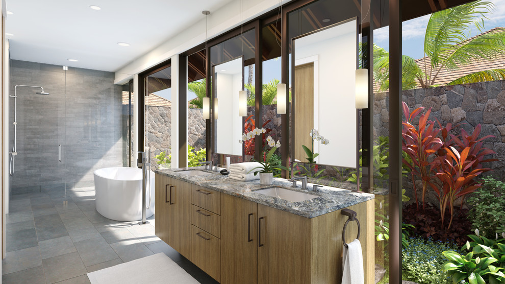 Photo of a medium sized world-inspired ensuite bathroom in Hawaii with a submerged sink, flat-panel cabinets, light wood cabinets, solid surface worktops, a freestanding bath, a built-in shower, a one-piece toilet, grey tiles, ceramic tiles, white walls and travertine flooring.