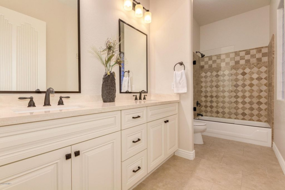 Photo of a classic family bathroom in Phoenix with raised-panel cabinets, beige cabinets, an alcove bath, a shower/bath combination, beige tiles, travertine tiles, porcelain flooring, a submerged sink, marble worktops, beige floors, a hinged door, beige worktops, double sinks and a built in vanity unit.