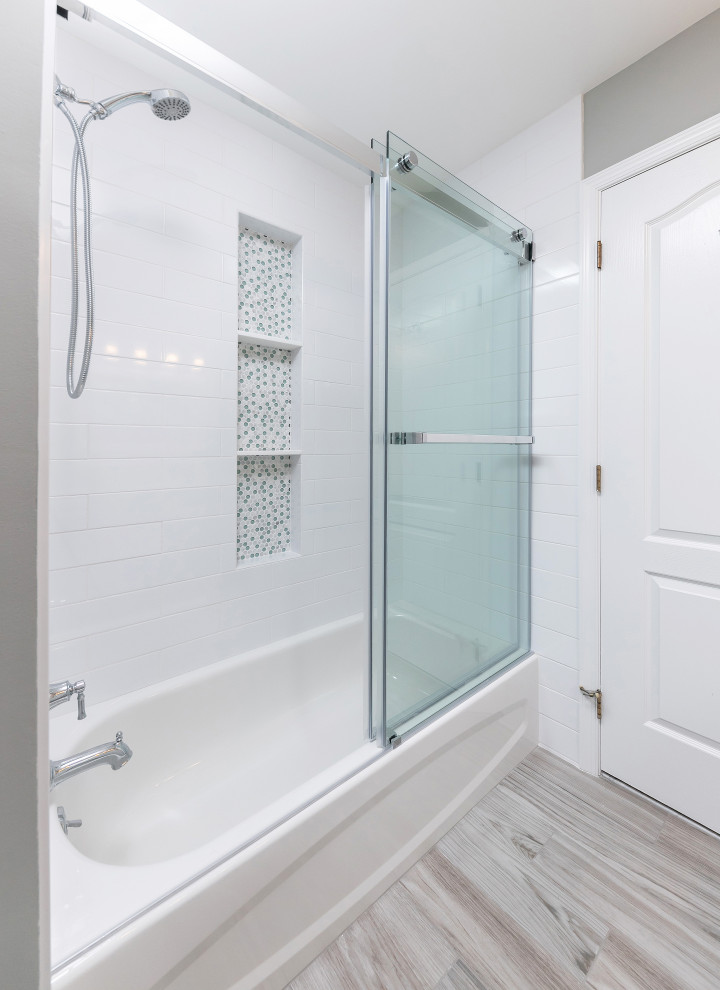 Cette photo montre une salle de bain de taille moyenne avec un placard avec porte à panneau surélevé, une baignoire en alcôve, un combiné douche/baignoire, un carrelage blanc, un carrelage métro, un mur blanc, sol en stratifié, un lavabo encastré, un sol gris, une cabine de douche à porte coulissante et un plan de toilette blanc.
