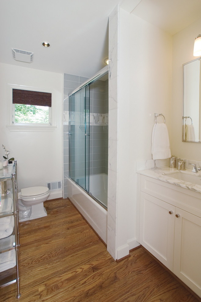 Idéer för att renovera ett litet vintage badrum, med luckor med infälld panel, vita skåp, marmorbänkskiva, ett badkar i en alkov, vit kakel, vita väggar och mellanmörkt trägolv