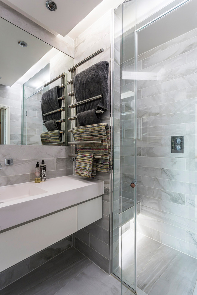Inspiration for a small contemporary ensuite bathroom in Surrey with glass-front cabinets, grey tiles, ceramic tiles, ceramic flooring, solid surface worktops, grey floors, a hinged door, white worktops, a built-in shower, grey walls and an integrated sink.