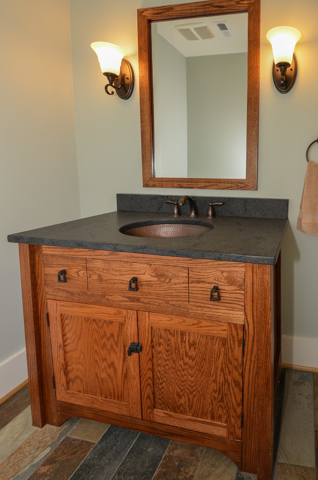 Cette image montre une salle de bain craftsman en bois brun avec un lavabo encastré, un placard à porte shaker, un plan de toilette en granite, un carrelage gris, des carreaux de porcelaine, un mur vert et un sol en carrelage de porcelaine.
