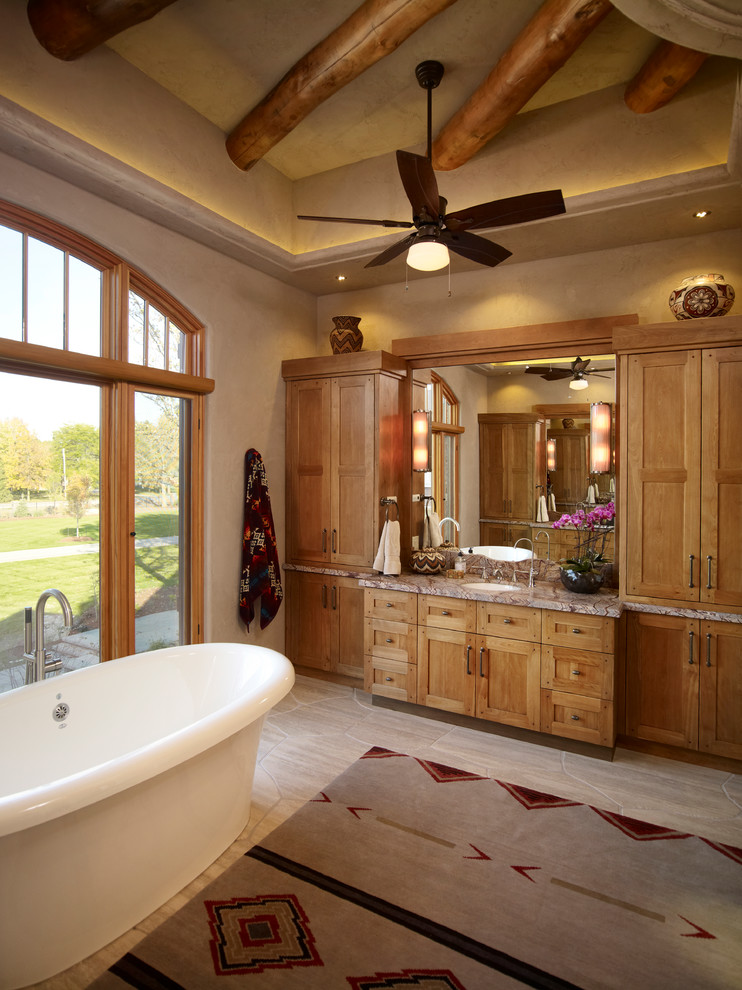 Пример оригинального дизайна: главная ванная комната в стиле фьюжн с фасадами с утопленной филенкой, светлыми деревянными фасадами, столешницей из гранита, отдельно стоящей ванной, бежевыми стенами и полом из керамической плитки
