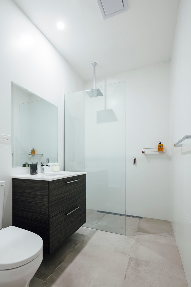 Inredning av ett modernt litet badrum, med släta luckor, svarta skåp, en öppen dusch, en toalettstol med separat cisternkåpa, vit kakel, porslinskakel, vita väggar, skiffergolv, ett undermonterad handfat och bänkskiva i akrylsten