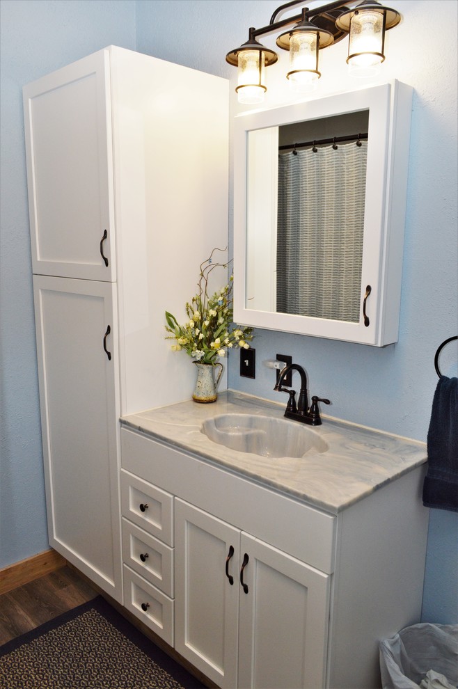 Foto på ett litet lantligt blå badrum med dusch, med skåp i shakerstil, vita skåp, en dusch i en alkov, ett integrerad handfat, marmorbänkskiva, brunt golv, dusch med skjutdörr och blå väggar