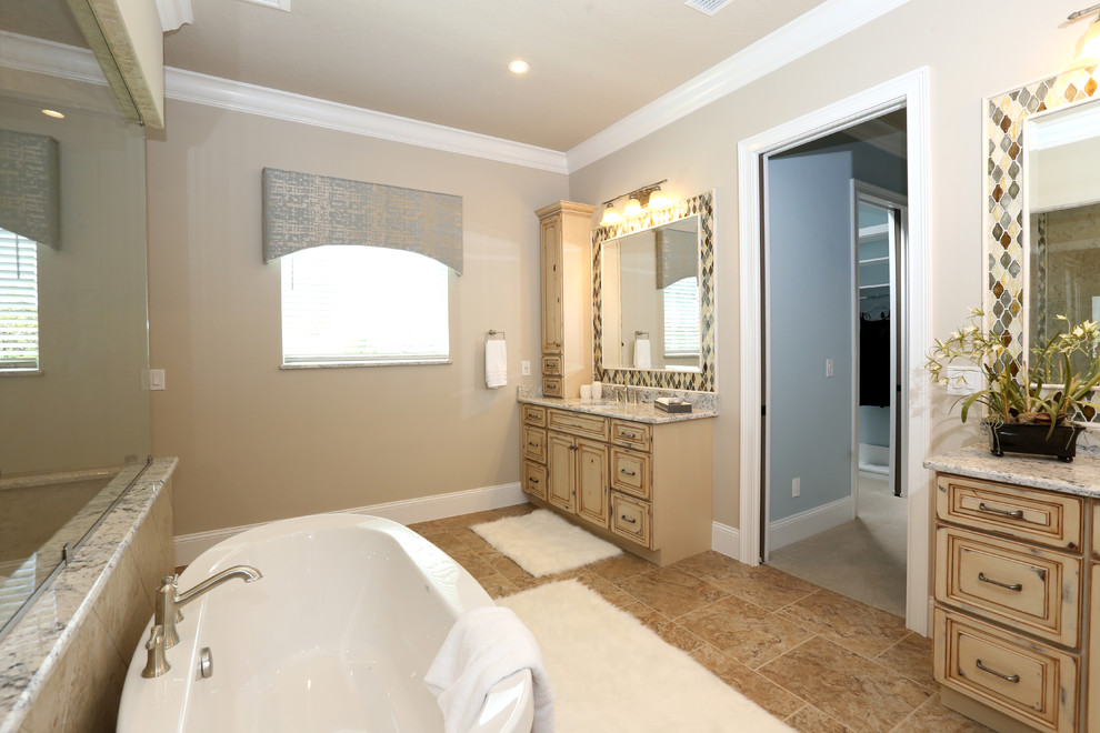 Bathroom - large traditional master beige tile and ceramic tile porcelain tile and beige floor bathroom idea in Orlando with raised-panel cabinets, distressed cabinets, a two-piece toilet, beige walls, an undermount sink and granite countertops
