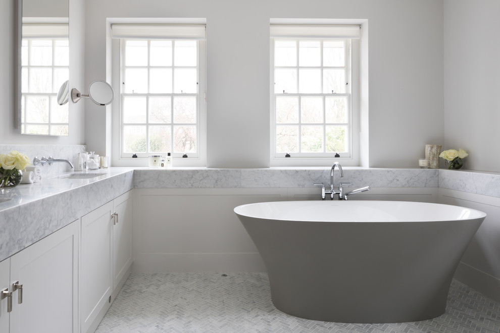 Idées déco pour une salle de bain classique avec un placard à porte shaker, des portes de placard blanches, une baignoire indépendante, un mur blanc, un sol en marbre, un lavabo encastré, un plan de toilette en marbre, un sol blanc et un plan de toilette blanc.