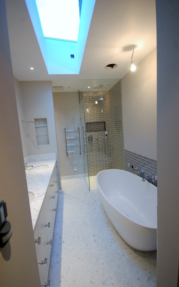 Photo of a medium sized contemporary ensuite bathroom in London with a submerged sink, flat-panel cabinets, white cabinets, marble worktops, a built-in bath, a walk-in shower, a wall mounted toilet, grey tiles, ceramic tiles, grey walls and mosaic tile flooring.