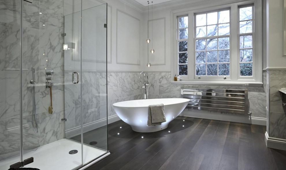 This is an example of a large traditional grey and brown family bathroom in London with a walk-in shower, marble tiles, white walls, dark hardwood flooring, marble worktops, brown floors, wainscoting, a freestanding bath, grey tiles, a hinged door, grey worktops and feature lighting.